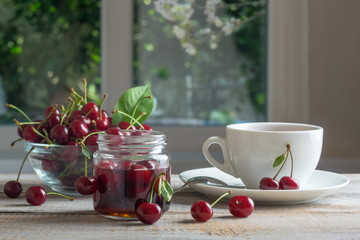 Tea and cherry jam on a wooden table. Sweet ripe berries in bowl. Delicious breakfast. Selective focus