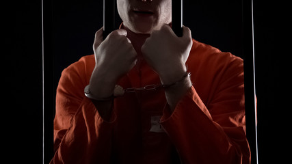 Convicted man in handcuffs holding prison bars, punishment for financial fraud