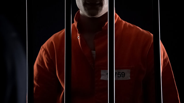 Convicted murderer standing against prison bars, imprisoned for kidnapping