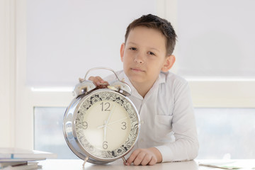 boy student teenager sitting at the table with textbooks and notebooks alarm clock on the window background . teen learns thinks the idea of a large clock .