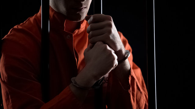 Arrested man in handcuffs behind bars feeling angry about failed robbery plan