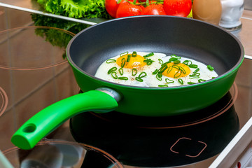 green pan with scrambled eggs from two eggs on a glass-ceramic stove in the kitchen