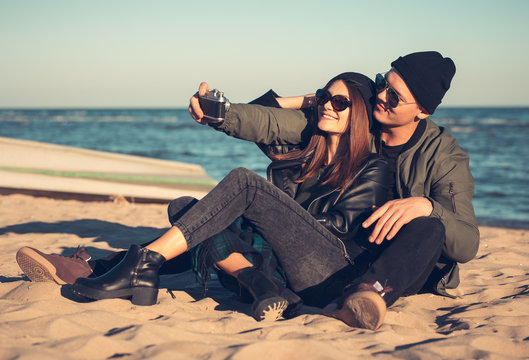 A young loving couple spends fun time by the sea and makes selfies. Man and woman have spring clothes