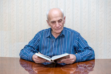 elderly man sits at a table and reads a book carefully