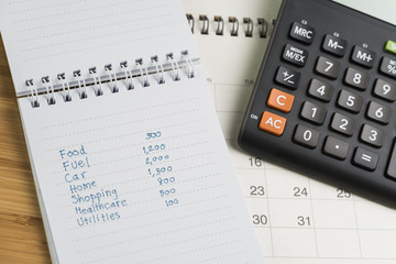 Expense and budget concept, list of expense in small notepad and calculator on desktop calendar on wooden table