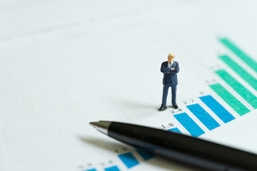Company growth, stock market return growing revenue and profit concept, miniature figure confidence businessman standing on bar chart and graph analysis report with black pen with copy space
