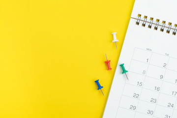 Flat lay or top view of clean white calendar with thumbtack or pushpin on vivid yellow background with copy space using as reminder, vacation plan, business organizer or meeting schedule concept © Nuthawut