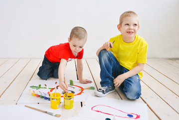 naughty creative children paint brush paints on paper funny colorful pictures on a wooden floor,...