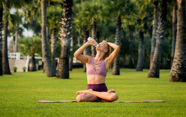 Beautiful young woman practic yoga at the beach. Early morning exercise. Drinking water. Sunrise