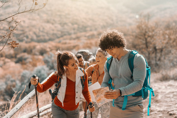 Hikers walking on glade. In foreground couple looking at map and searching for right direction. Autumn time.