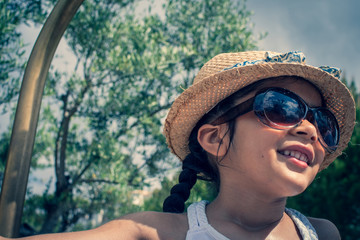 A 5 year old girl in a sunhat and sunglasses plays on the luggage rack of a bellboy, outside a holiday hotel, whilst on vacation. 