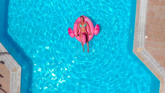 Young happy woman relaxing on inflatable pool toy in blue swimming pool on sunny day