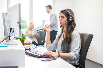 Confused costumer support operator woman with headphones trying to solve problem while working on...