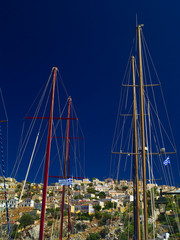 Simi island multi colored houses and masts from sail boats in the port.