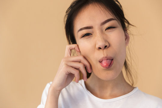 Photo of optimistic korean woman wearing basic t-shirt sticking out her tongue and looking at camera