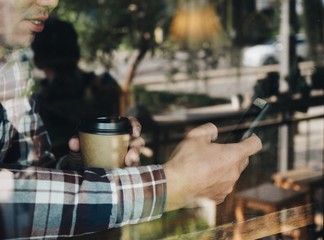 Cropped Asian man hands holding smart phone and coffee cup in cafe.