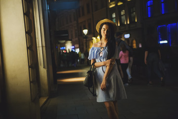 Fototapeta na wymiar Young woman in hat walking at night city centre