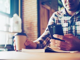 Cropped Asian man hands holding smart phone and coffee cup in cafe.