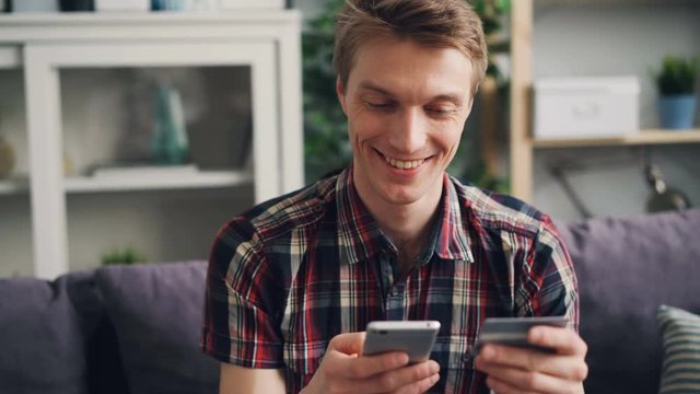 Cheerful young man is making online payment with bank card touching smartphone screen then smiling happily. Finance, internet shopping and youth concept.