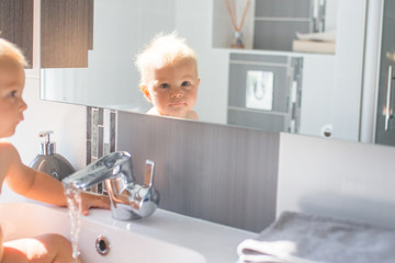 Obraz premium Baby taking bath in sink. Child playing with foam and soap bubbles in sunny bathroom with window. Little boy bathing. Water fun for kids. Hygiene and skin care for children