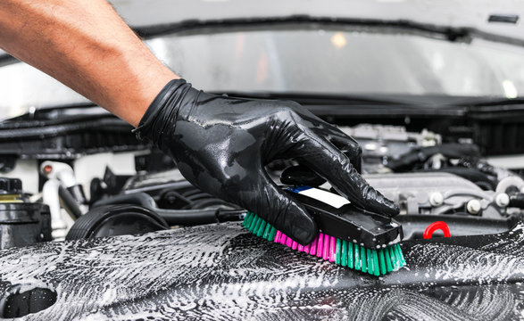 A man cleaning car engine with shampoo and brush. Car detailing or valeting concept. Selective focus. Car detailing. Cleaning with sponge. Worker cleaning. Car wash concept solution to clean