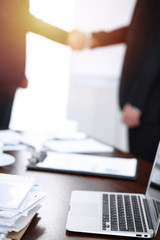 Documents and laptop on the table. Business people shaking hands on the background, silhouettes