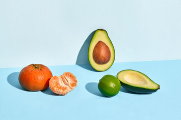 Composition of fresh fruits, mandarin lime and two halfs of cutted avocado on two-colored background