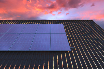 Solar panels modules on house roof with sunset sky in background