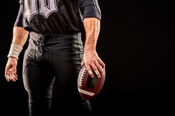 Mid section of American football player with ball against black, copy space