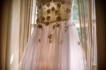 Elegant pink rose wedding dress with a train hanging on window. Wedding morning