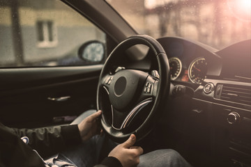 driver’s hands hold the steering wheel of a modern car while waiting for a passenger.