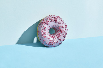 Food design. Close up high quality image of pink glazed donut on blue background