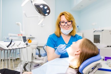 Woman dentist in blue uniform treats tools teeth girl lying on the couch. Inspection of the oral cavity in the dental clinic to create a beautiful smile and straight teeth