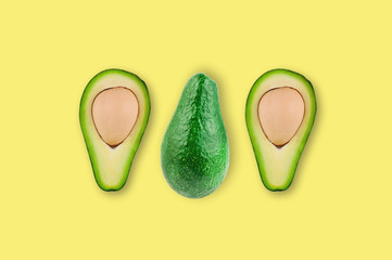 Row of fresh whole and halves of organic avocado with kernels in center of yellow table in kitchen or market. Top view. Cooking concept