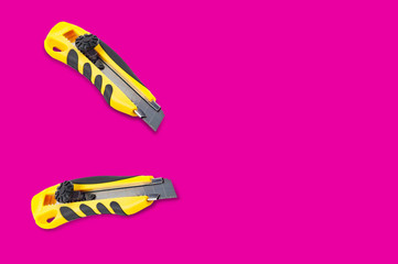 Pair of stationery knives with yellow and black plastic handle on pink background with copy space for your text