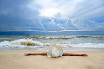 Fototapeta na wymiar Young girl in a white hat on the sea beach. Clean, sandy beach against the blue sea.