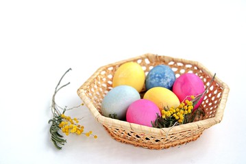 Multi-colored Easter eggs in a wicker basket on a white background. Selective focus.
