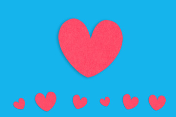 One big red paper heart and row of small hearts on blue table. Top view. Valentines Day concept