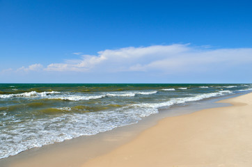 Sea waves wash the beach against a blue sky. Landscape on a wild beach. The sea in the summer.