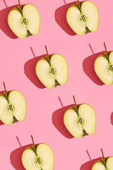 Colorful fruit pattern of fresh cutted apple halves with pits on coral pink background, top view