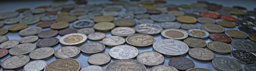 An elongated image with coins from different currencies laying on a white tile