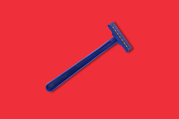 One male disposable plastic razor blue color with two sharp blades in center on red table in bathroom. Top view. Hygiene concept