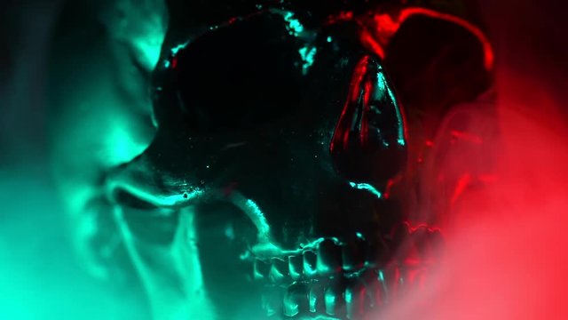 Shining skull head rotates from left to right on dark smoke background with neon red and green light. Halloween celebration, glamour, style concept. fear and horror