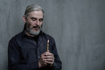 Senior man hands hold a candleon dark background. Space for text