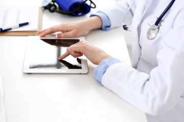 Doctor working table. Woman physician using tablet computer while sitting in hospital office close-up. Healthcare, insurance and medicine concept