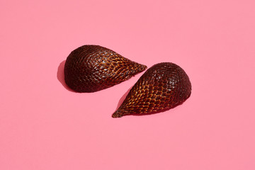 Close up high quality image of bronze salacca halves, fruit composition on pink pastel