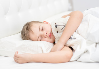 Young boy sleeping in bed with toy bear