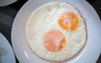 two fried egg on the white plate on breakfast table