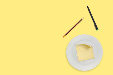 Blank square paper sticker with curved corner in white round plate near wooden pencil and black pen...