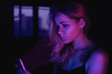 Fototapeta premium Girl using cellphone at night with neon light - pink and blue